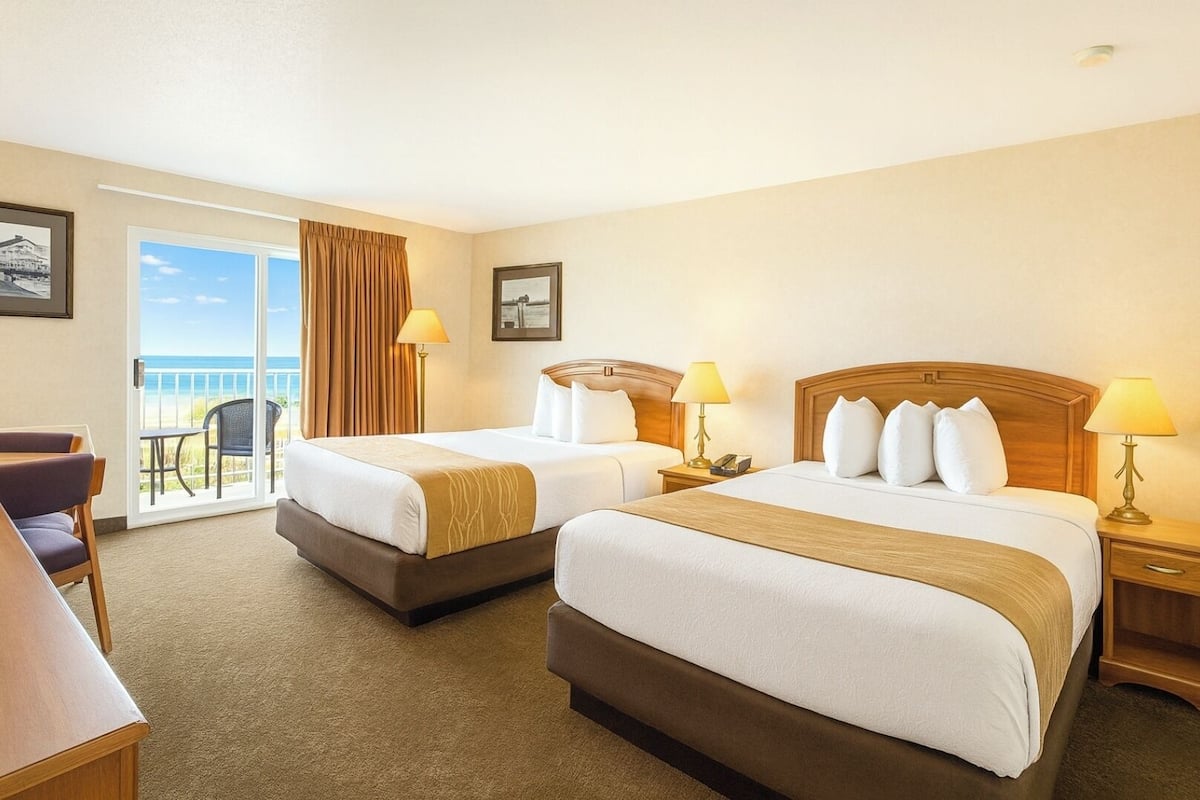 A hotel room with two beds, a balcony with a view, and a desk with a chair.