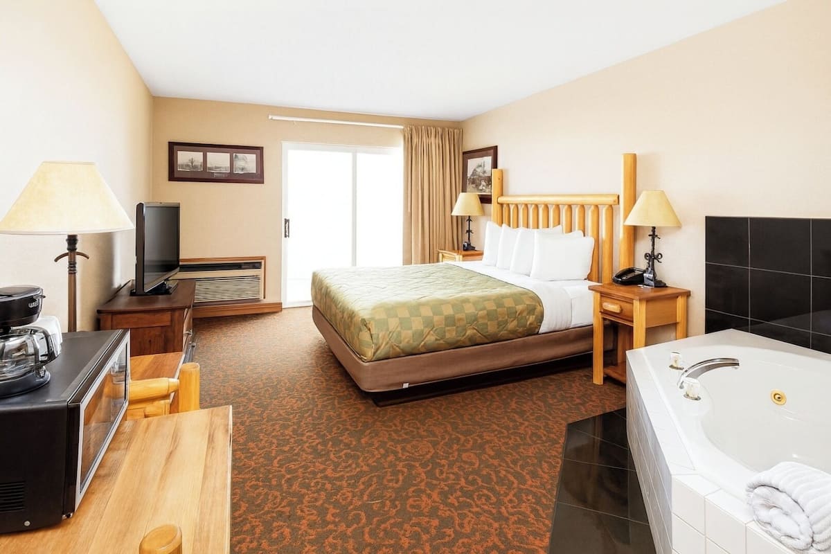 A hotel room with a bed, a desk with a coffee maker, a TV, a bathroom with a bathtub, and a large window.