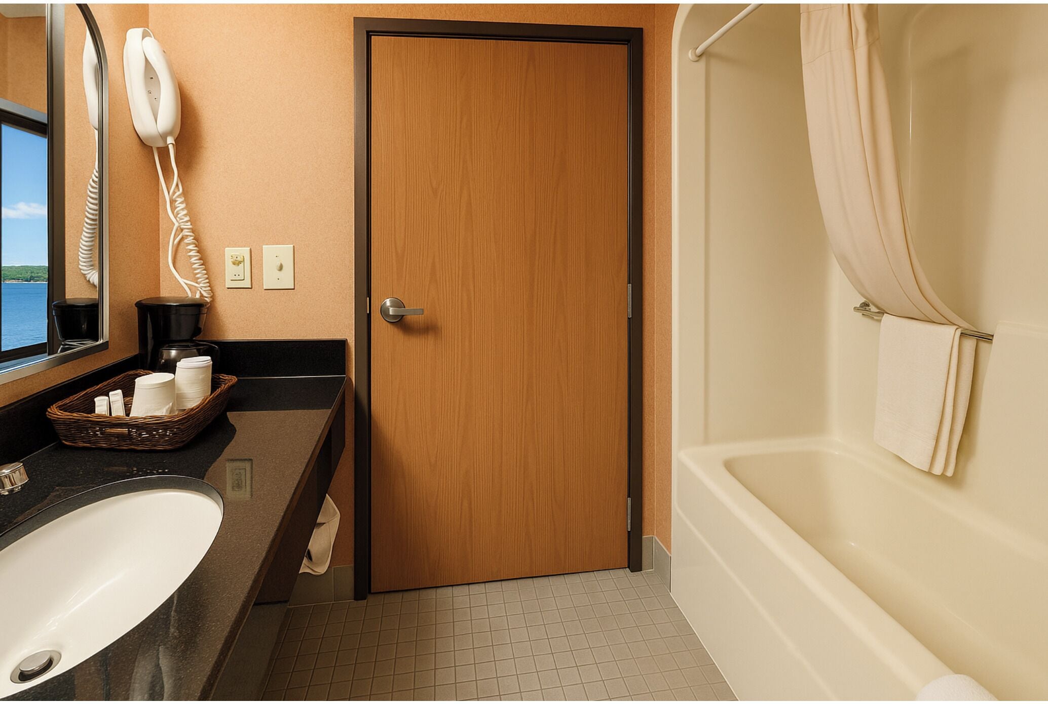 A hotel bathroom with a wooden door, a sink, a bathtub, and a telephone on the wall.