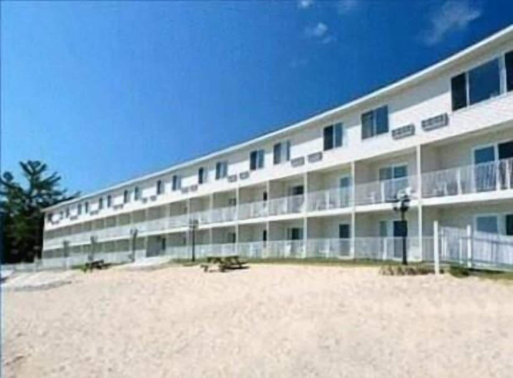 A multi-story motel with balconies on each floor, located on a sandy beach.