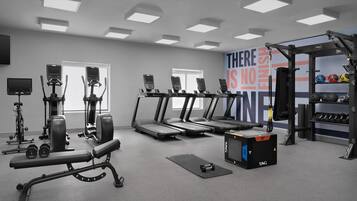 Une salle de sport équipée de tapis de course, d’appareils de musculation et d’un mur orné de messages motivants.