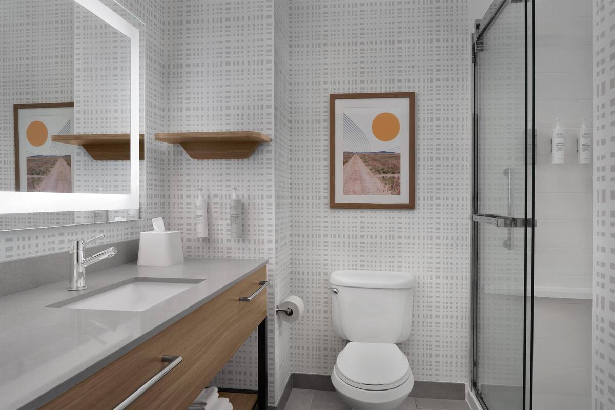 A modern bathroom with a large mirror, a sink, a toilet, and a shower area.