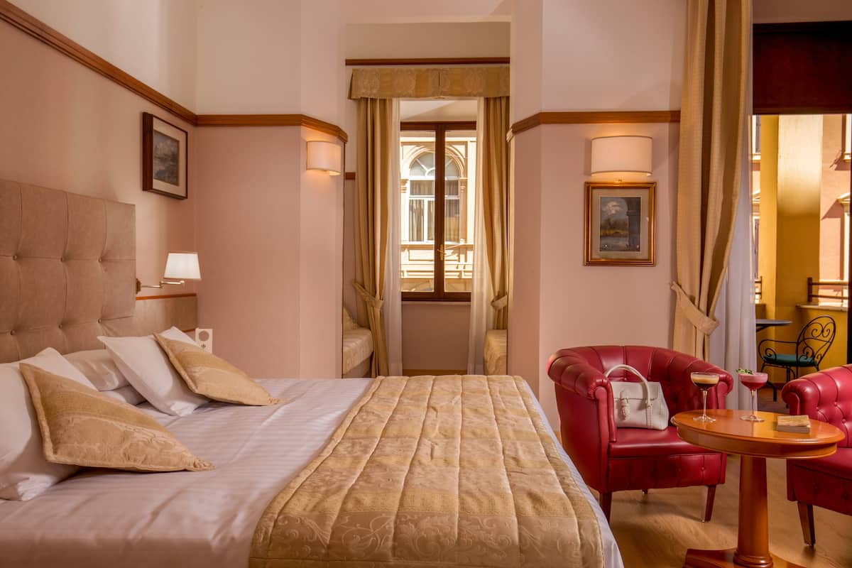 A hotel room with a large bed, a red leather armchair, a small round table, and a view of the room's interior.