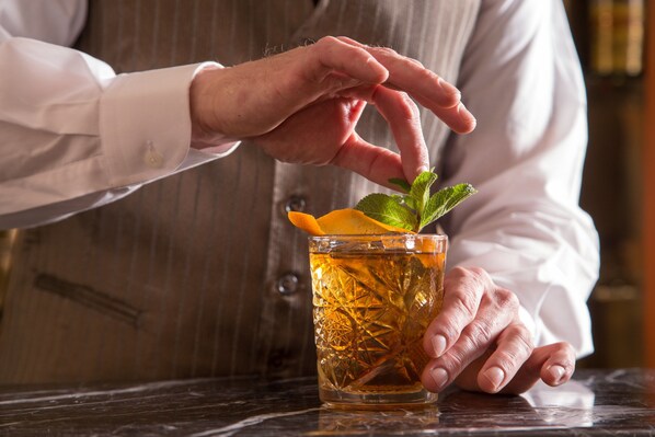 A person holding a glass with a mint leaf garnish. - Hotel La Residenza (Rome)