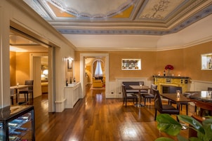 Un espacio amplio con piso de madera, una zona de comedor con mesa y sillas, una barra con mostrador y estanterías, y un techo decorativo con diseños intrincados.