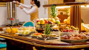 Un bufé con diversas frutas, pasteles y una piña como pieza central.