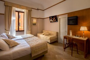A hotel room with two beds, a desk, and a chair. There is a TV mounted on the wall, a door, and a window with curtains.