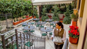 Un patio de hotel con varias mesas redondas y sillas, rodeado de abundante follaje y plantas en macetas.