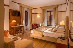 A hotel room with a bed, bedside table, lamp, chair, desk, and a TV mounted on the wall.