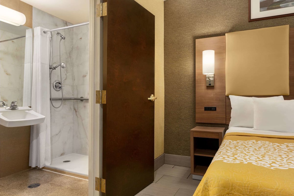 Habitación de hotel con ducha, lavabo, mesita de noche y cama con cabecera.