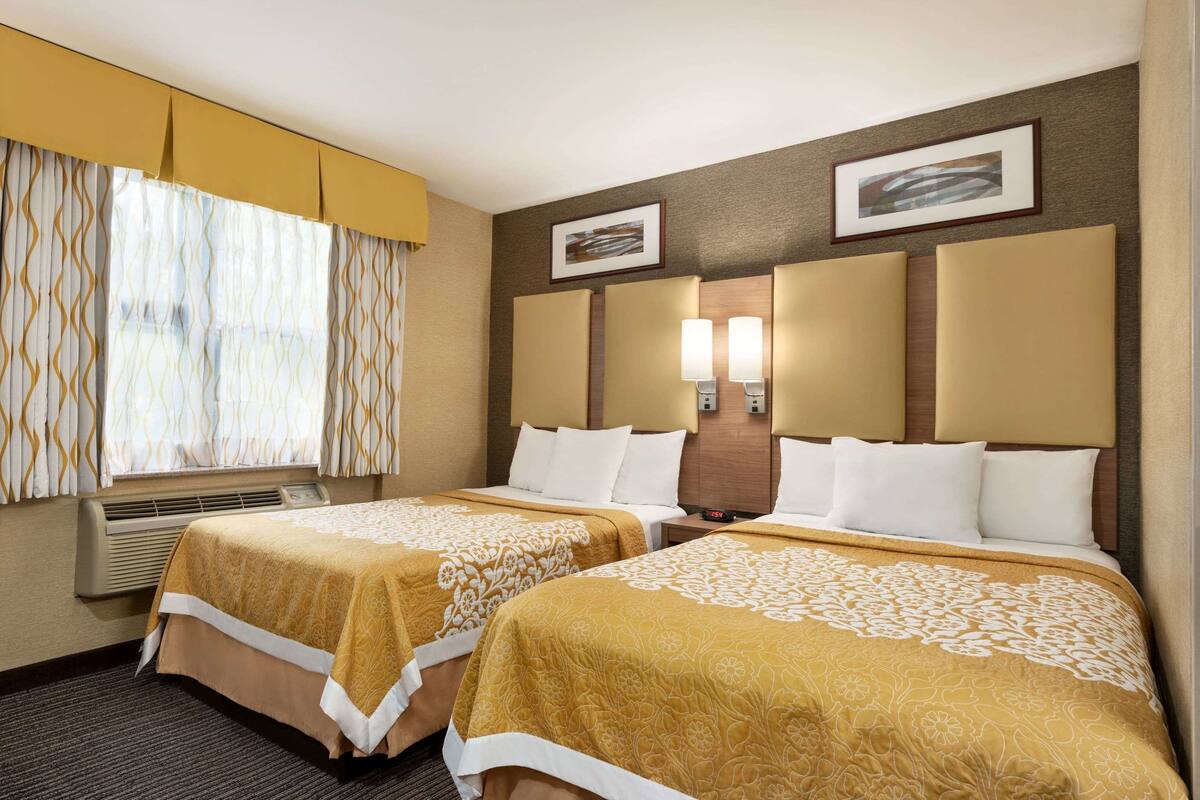 Habitación de hotel con dos camas, una ventana con cortinas, un aire acondicionado de pared y dos lámparas de pared.