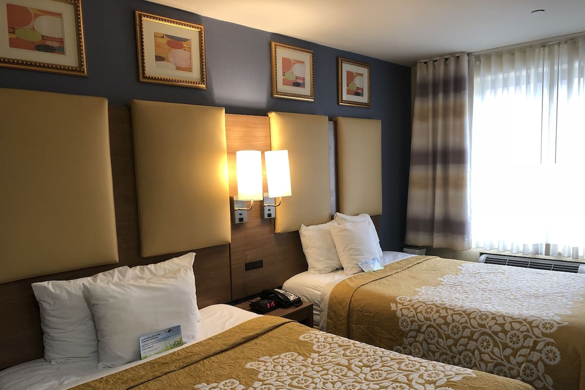 Habitación de hotel con dos camas, una mesita de noche con un teléfono y un reloj, y luces fijadas a la pared.
