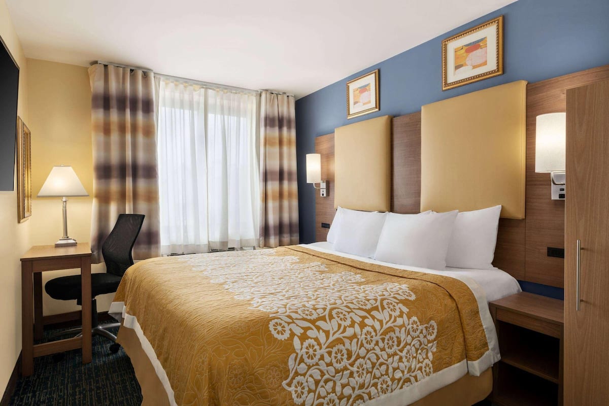 Habitación de hotel con cama, escritorio, silla, lámpara y ventana con cortinas.