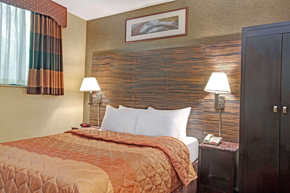 A hotel room with a large bed, two bedside lamps, a telephone, and a wardrobe.