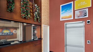Zona de recepción con el letrero de Days Inn, un mostrador de recepción, un arreglo floral en la pared y una puerta con vistas al cielo.