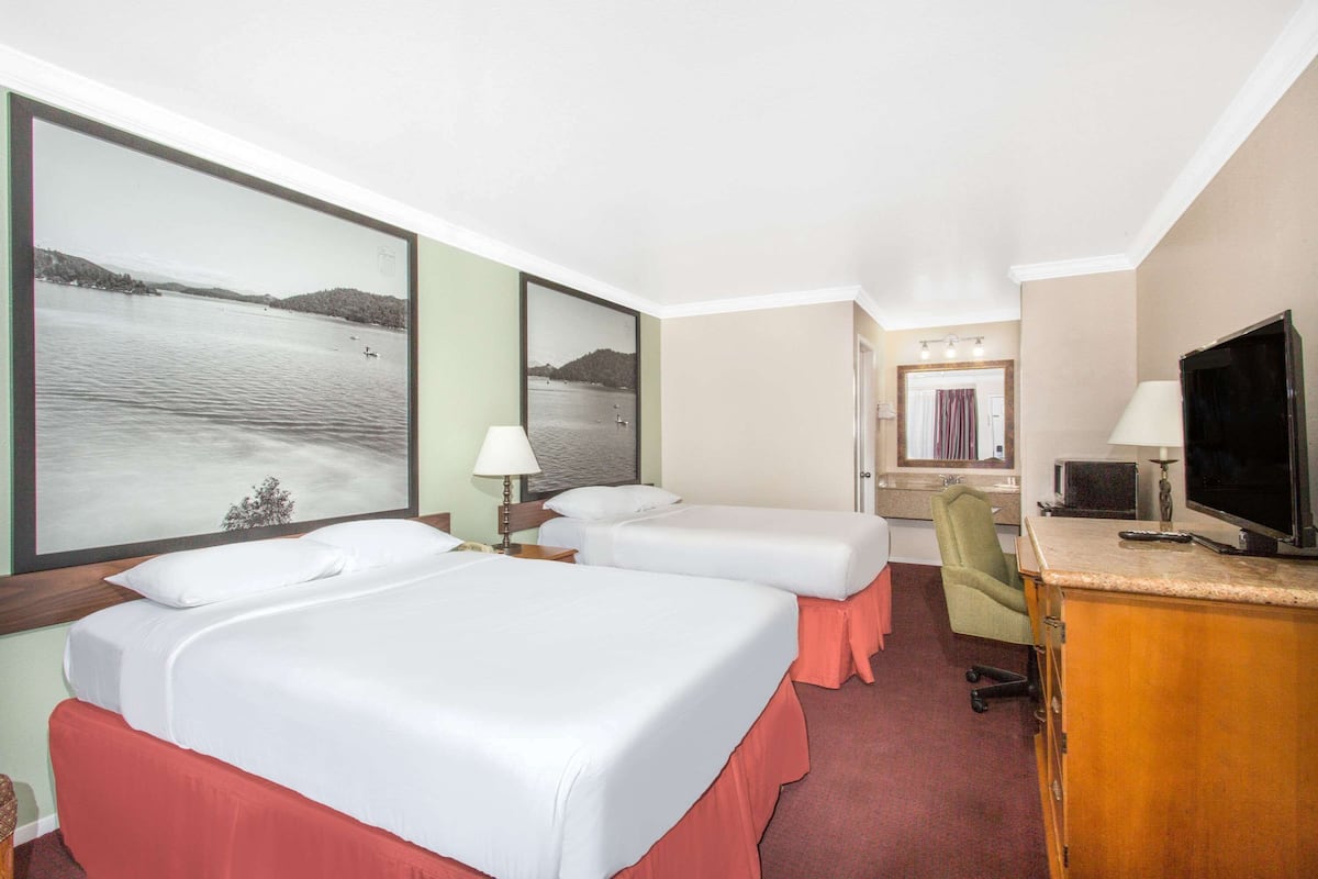 Habitación de hotel con dos camas, un escritorio, un televisor y un ventanal con vista al lago.