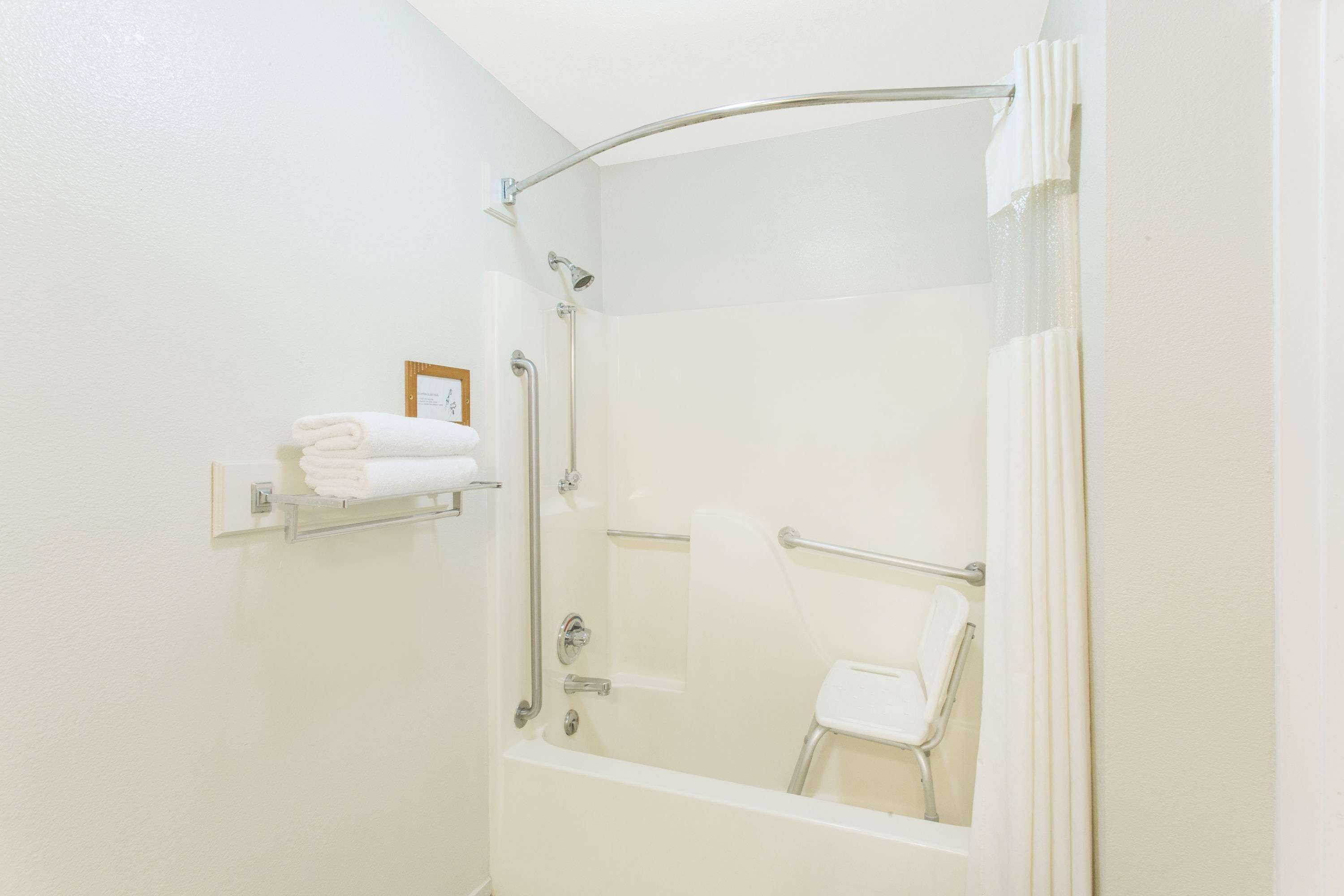Une salle de bain blanche avec une douche, des toilettes et un porte-serviettes sur lequel sont pliées des serviettes.