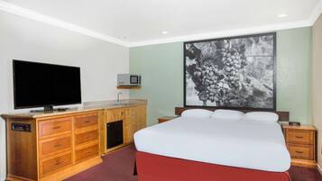 A hotel room with a bed, a TV, a wooden dresser, and a wall-mounted picture.