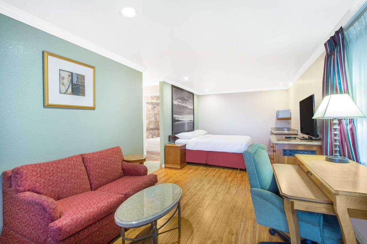 Habitación de hotel con sofá rojo, una mesita, cama con ropa de cama blanca, escritorio con lámpara y televisor.
