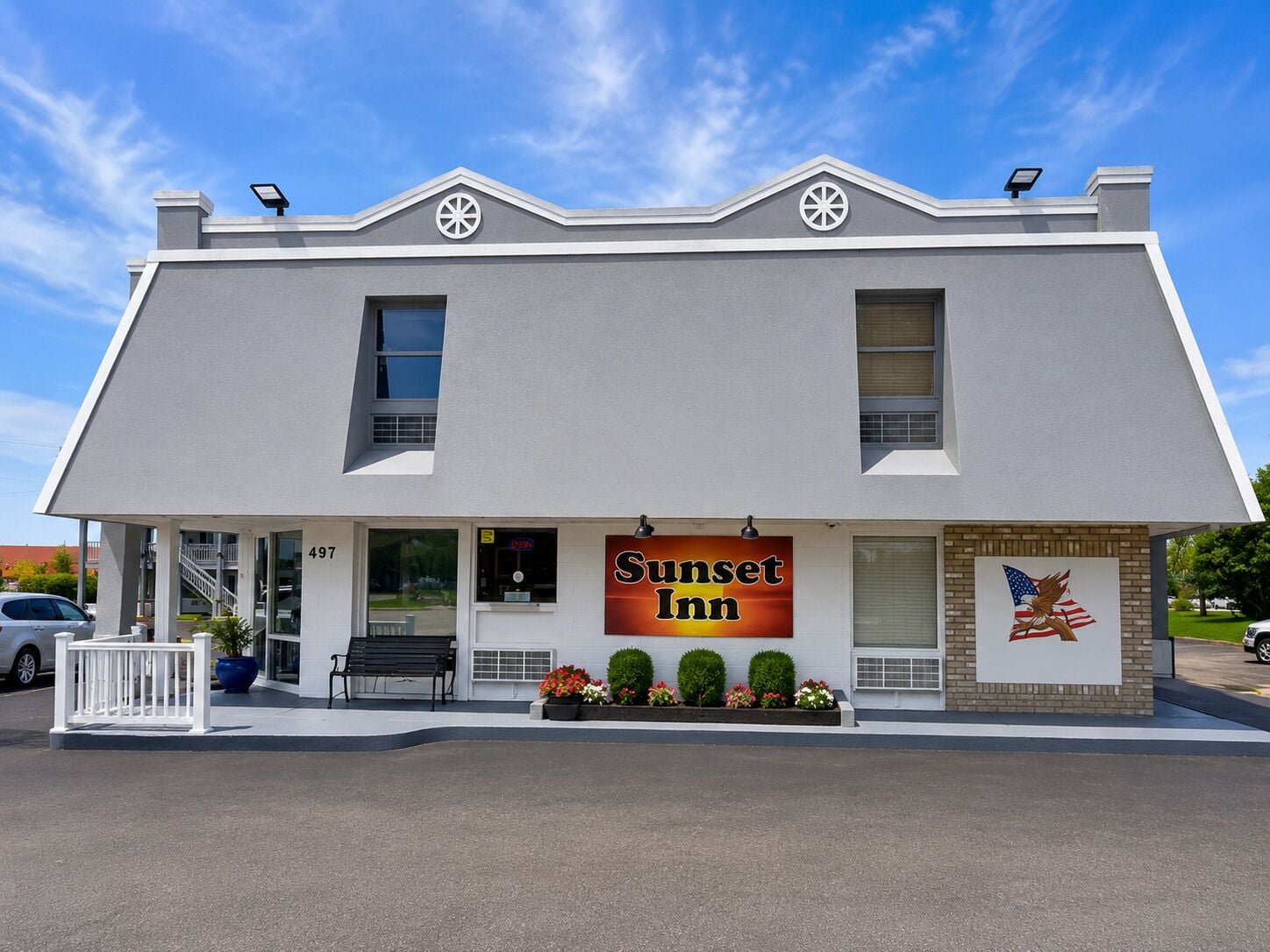 A two-story building with a sign reading 'Sunset Inn.' There are two windows on the upper floor, a door on the ground floor, and a bench outside.