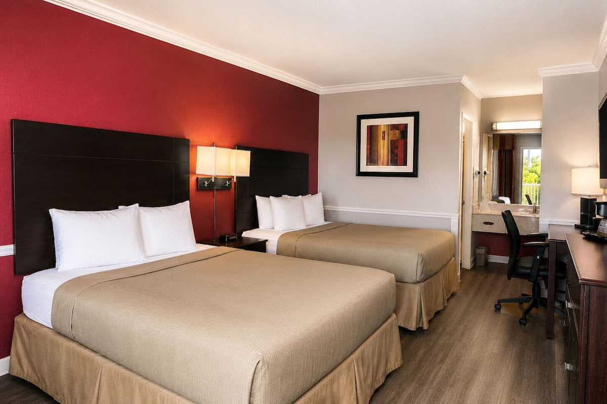 A hotel room with two beds, a desk, a chair, and a bathroom visible through an open door.