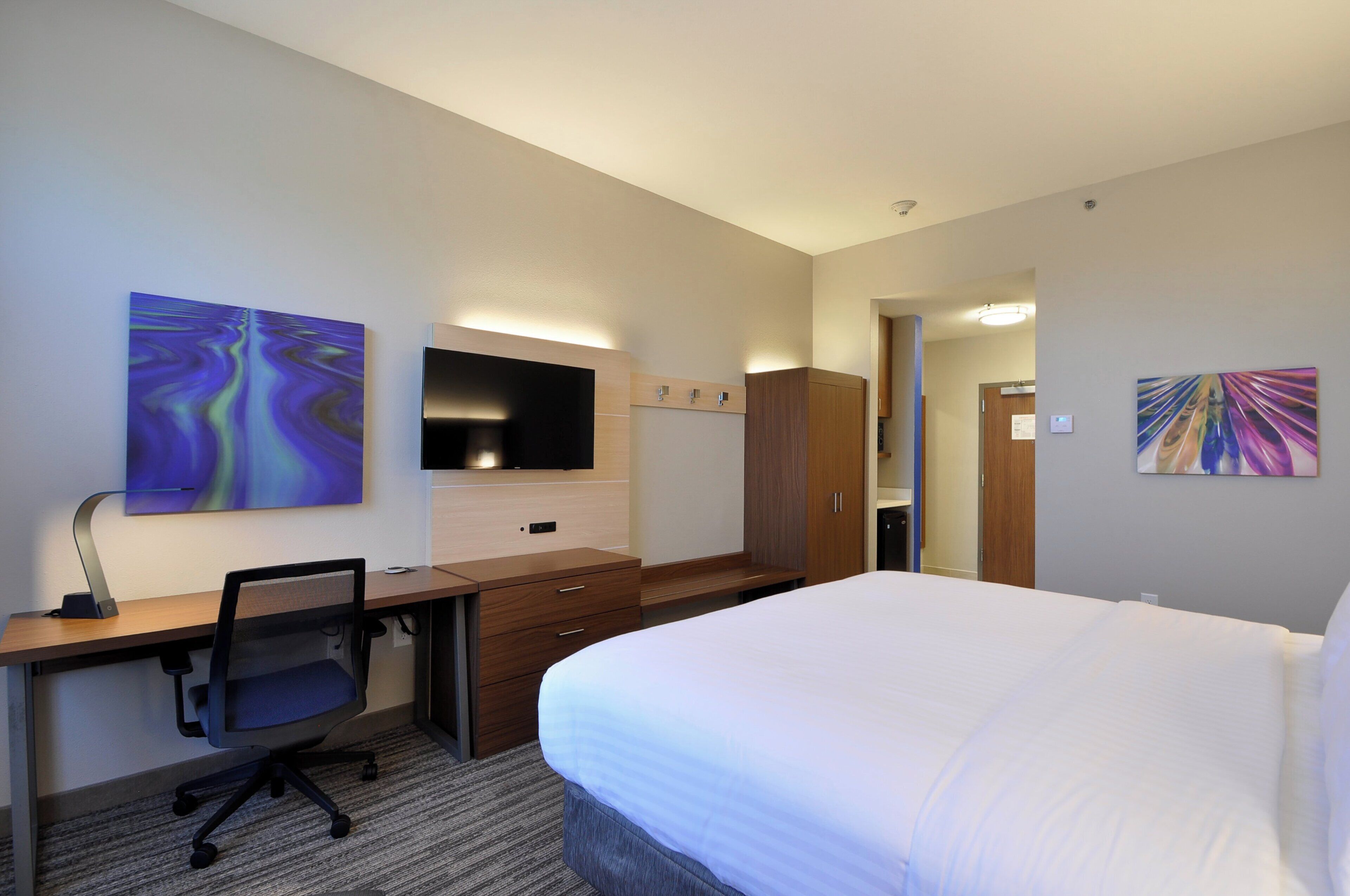 Habitación de hotel con cama, escritorio, silla, televisión y obras de arte en las paredes.