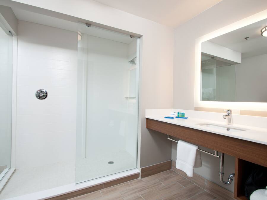 A modern bathroom with a glass-enclosed shower, a white sink with a wooden vanity, and a large mirror above the sink.