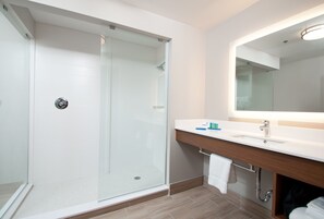 Une salle de bain moderne avec une douche à parois de verre, un lavabo blanc avec un meuble-vasque en bois et un grand miroir au-dessus du lavabo.