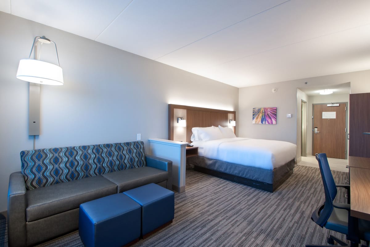 A hotel room with a bed, a sofa, a desk, and a lamp.