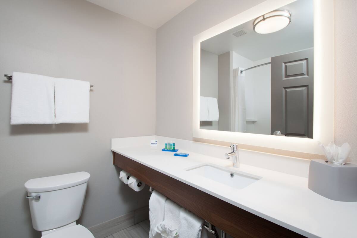 A modern bathroom with a white toilet, a sink with a mirror above it, and a towel rack above the toilet.