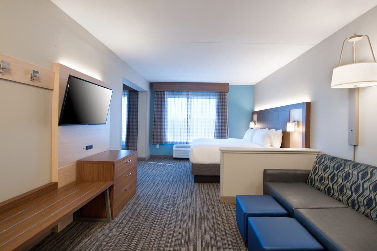 A hotel room with a bed, a sofa, a TV, a desk, and a window with curtains.