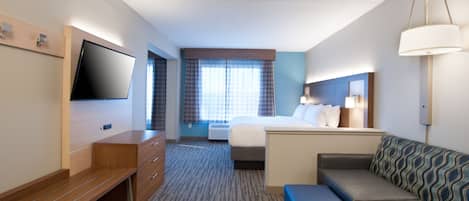 A hotel room with a bed, a sofa, a TV, a desk, and a window with curtains.