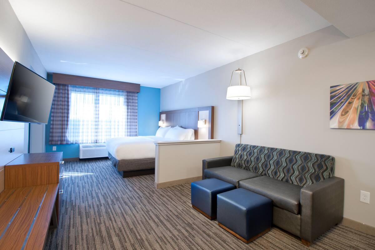 A hotel room with a bed, a sofa, a TV, a desk, and a lamp.