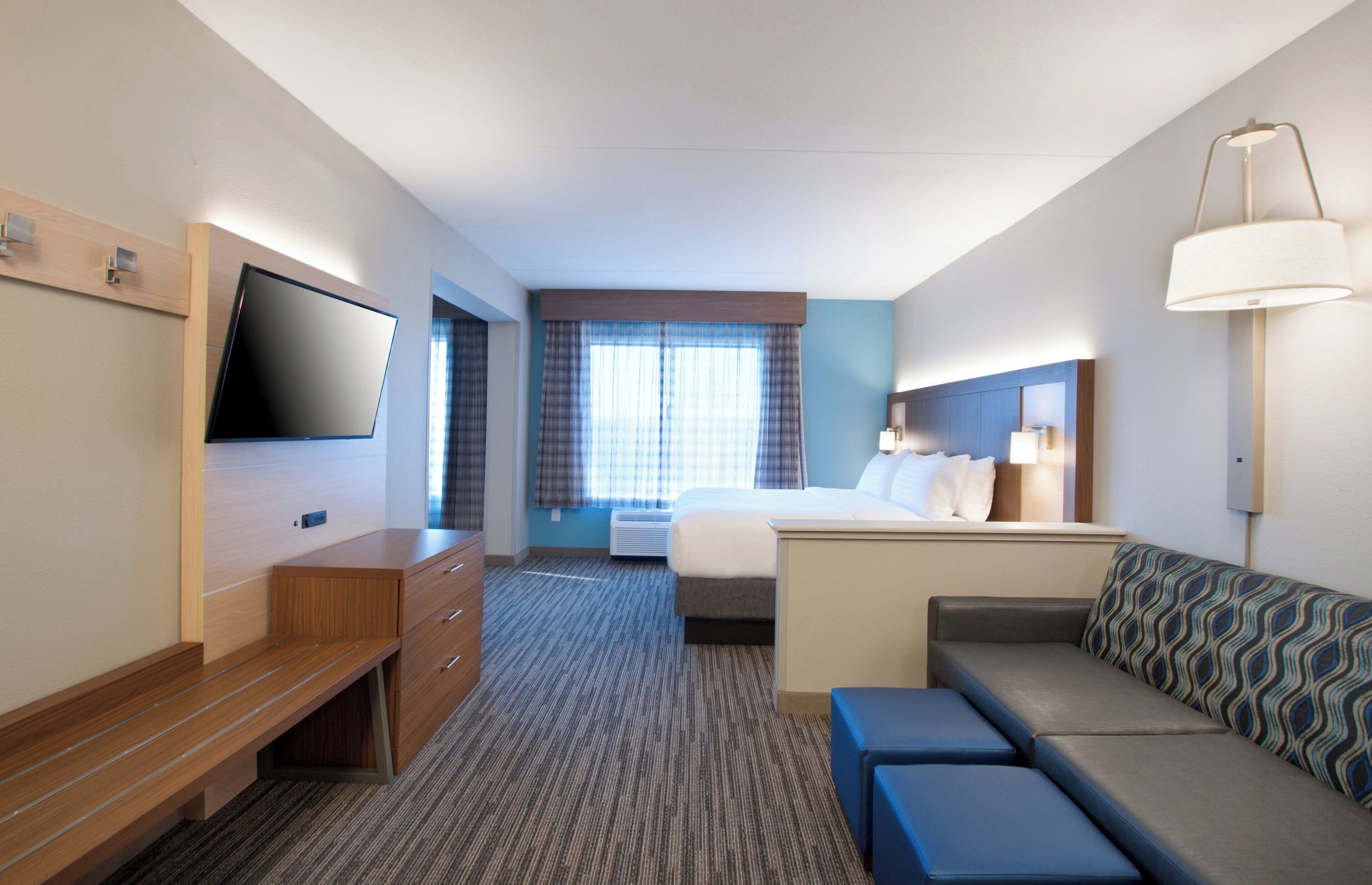 A hotel room with a bed, a desk, a television, a sofa, and a window with curtains.