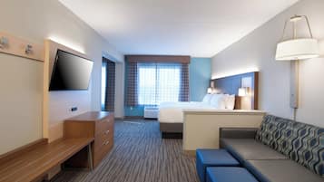 A hotel room with a bed, a desk, a television, a sofa, and a window with curtains.