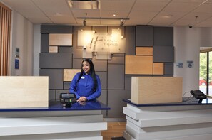 Een hotel receptie met een digitaal incheckkiosk, een Holiday Inn Express bord en een bordje 'niet roken'.