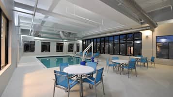 Un área de piscina interior con piscina, sillas y mesas azules.