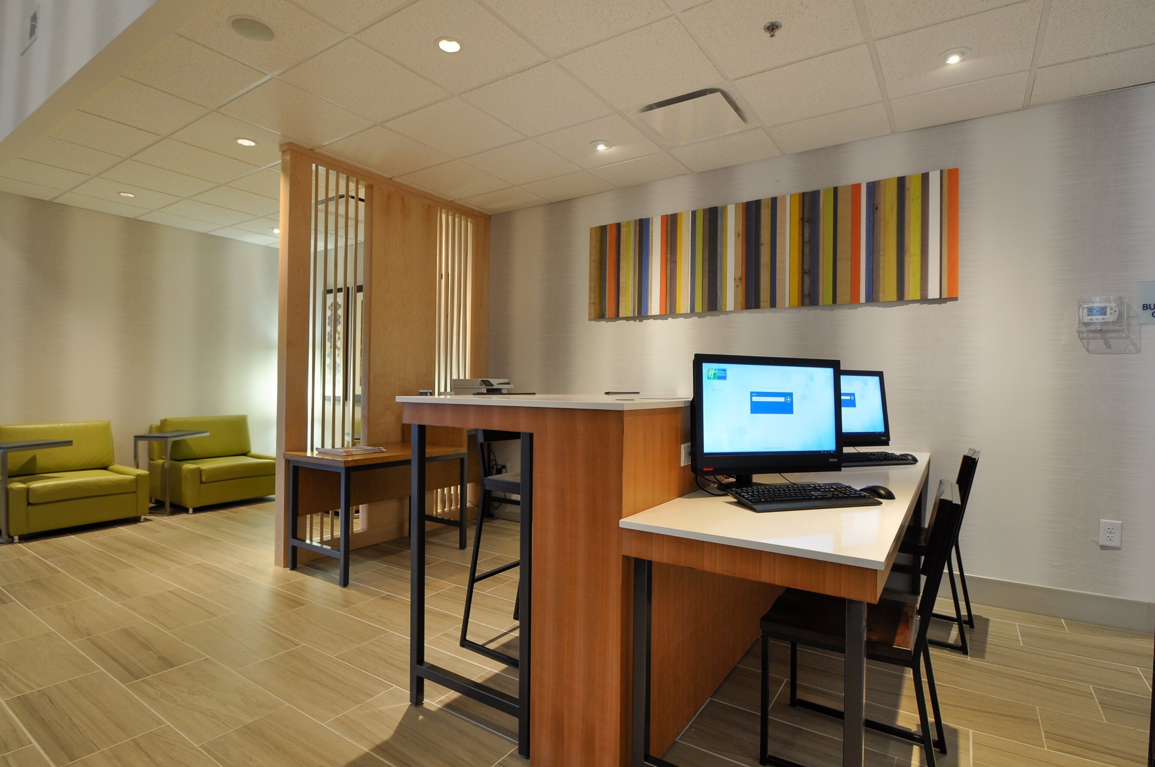 A modern office space with a reception desk, two computer monitors, a printer, and a seating area with two green chairs.