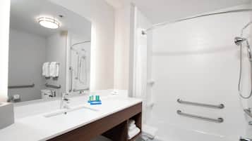 A modern bathroom with a large mirror, a white sink, a vanity with a towel rack, and a separate shower area with a handheld showerhead.