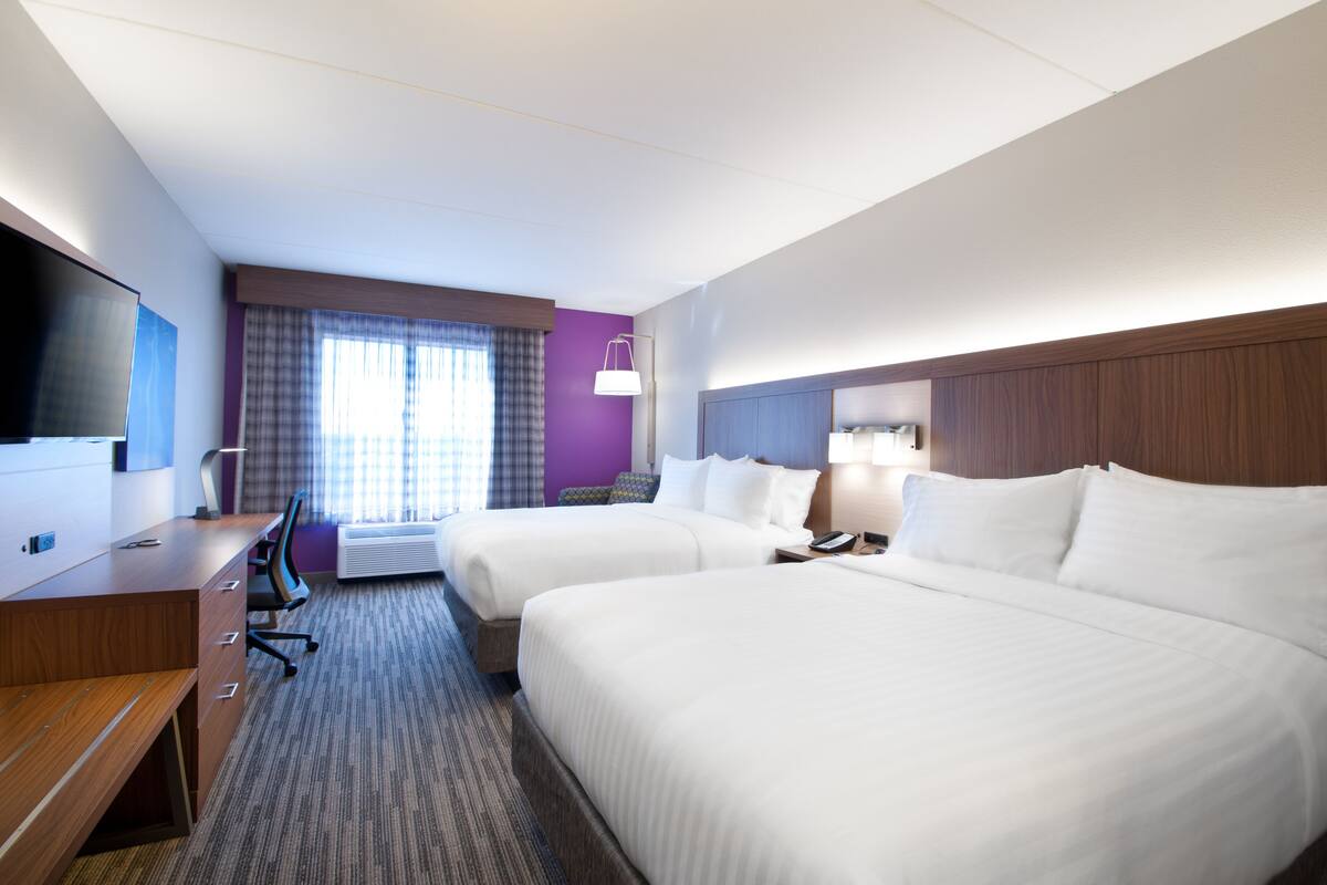 A hotel room with two beds, a desk, a TV, and a window with curtains.