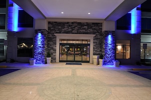 Entrada de hotel con fachada de piedra, puertas de cristal e iluminación azul.