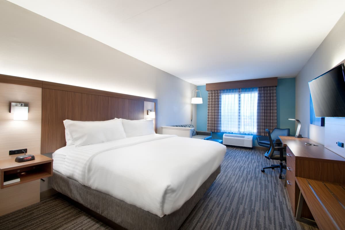 A hotel room with a large bed, a desk, a chair, a TV, and a window with curtains.