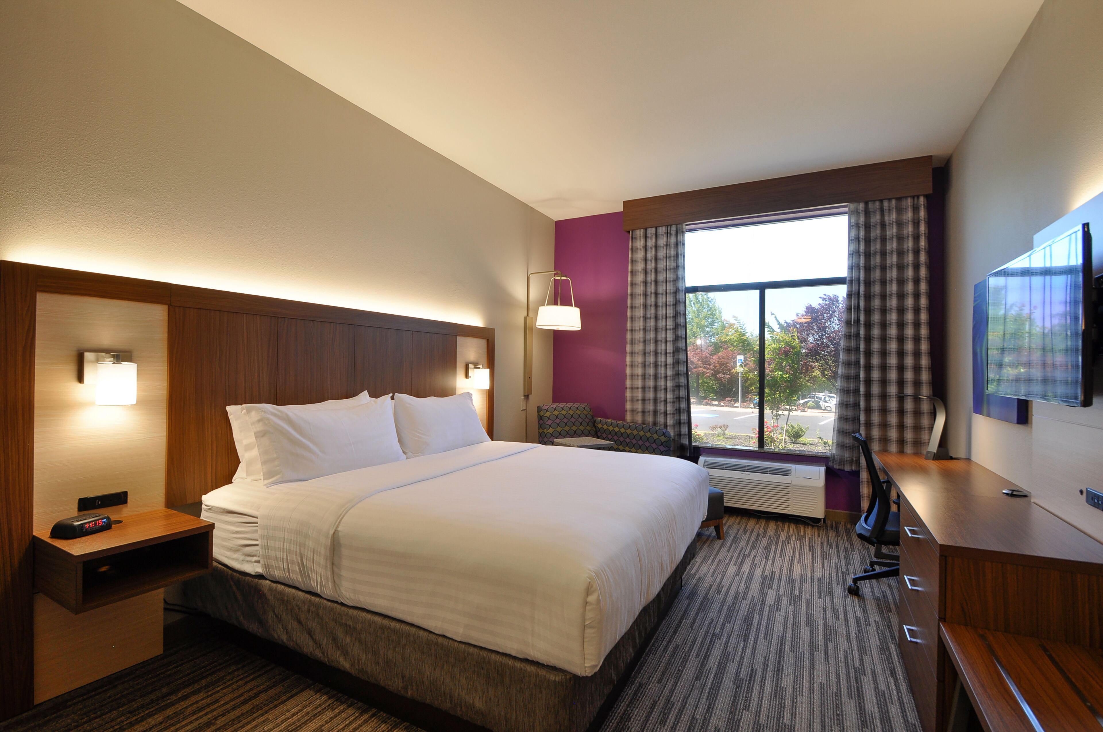 Hotelkamer met een groot bed, een bureau, een stoel, een televisie en een raam met gordijnen.