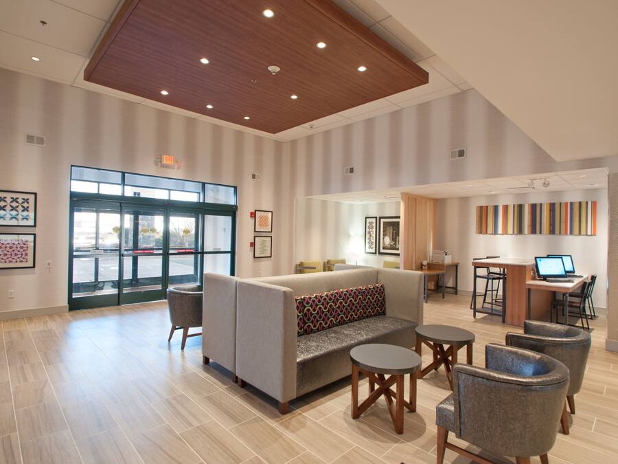 Eine großzügige Lobby mit modernem Design, ausgestattet mit einer Couch, Sesseln, einem Couchtisch und einer Rezeption mit Computern.