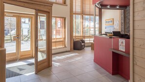 A modern hotel lobby with a reception desk, a seating area, and large windows with blinds. - Pierre & Vacances Residence Le Christiana (Courchevel)