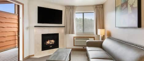 Ein Wohnzimmer mit Kamin, einem an der Wand befestigten Flachbildfernseher, einer Couch und einem Fenster mit Vorhängen.