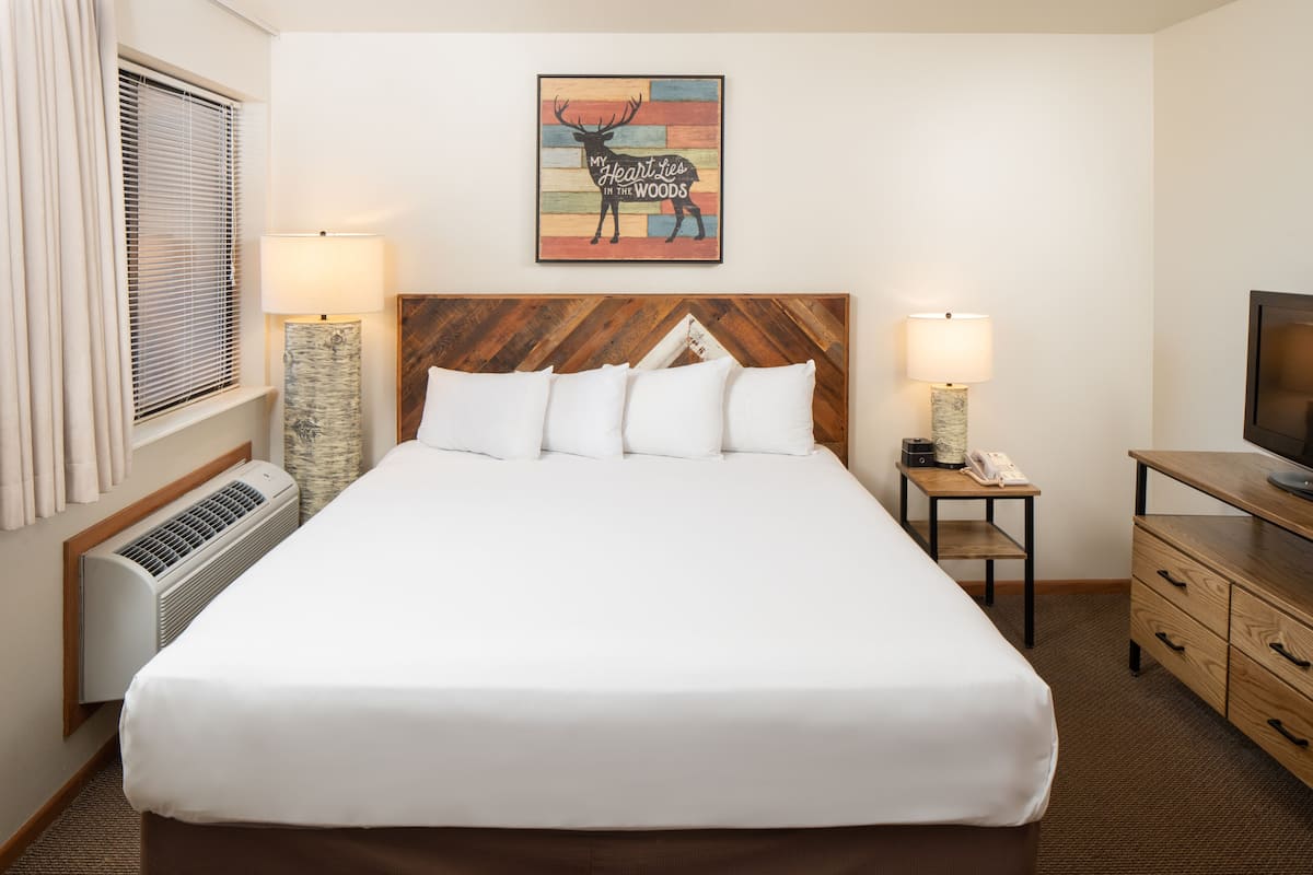 A hotel room with a large bed, two bedside tables, a TV, and a painting on the wall.