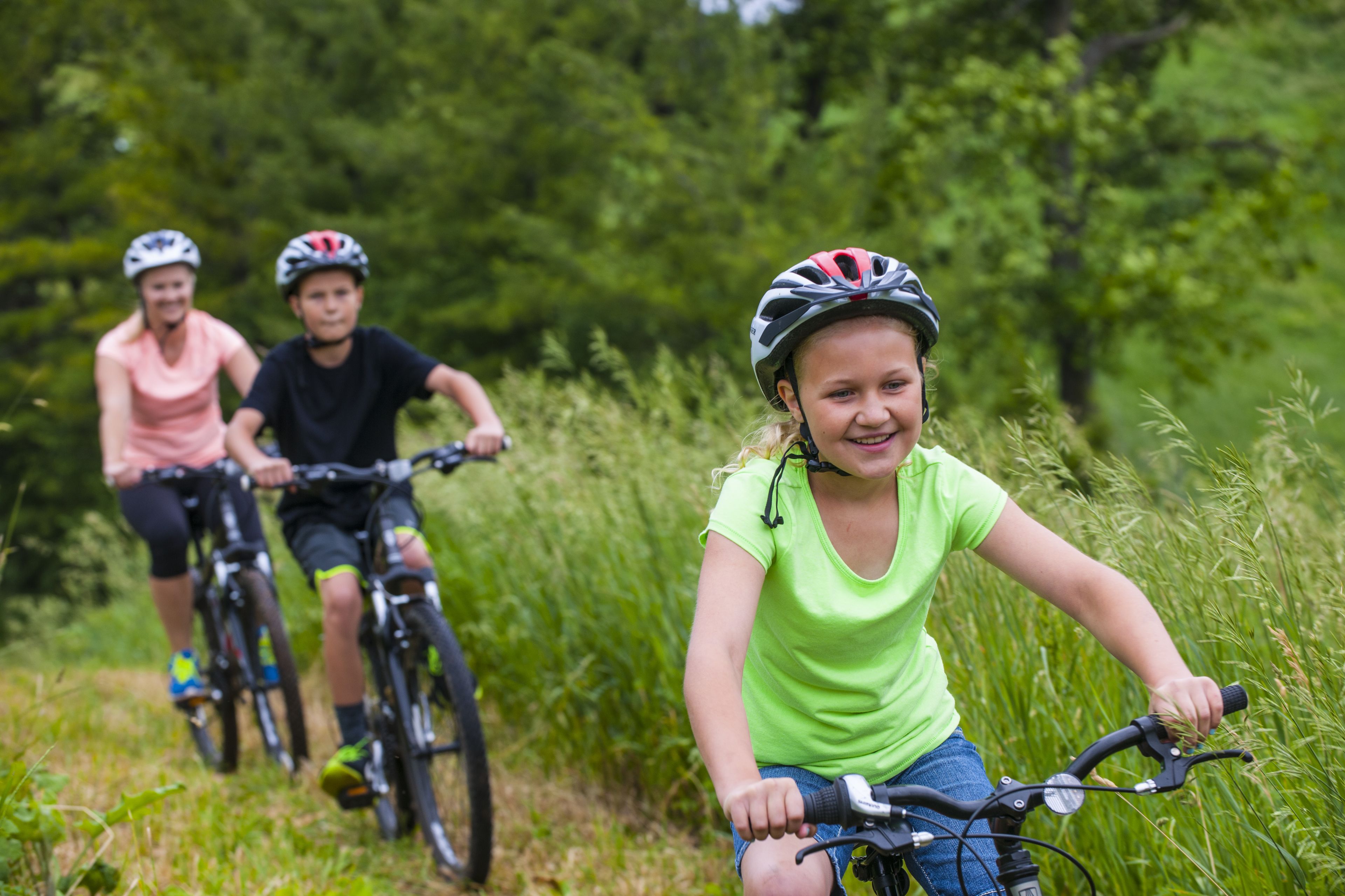 Three people riding bicycles on a trail surrounded by greenery.