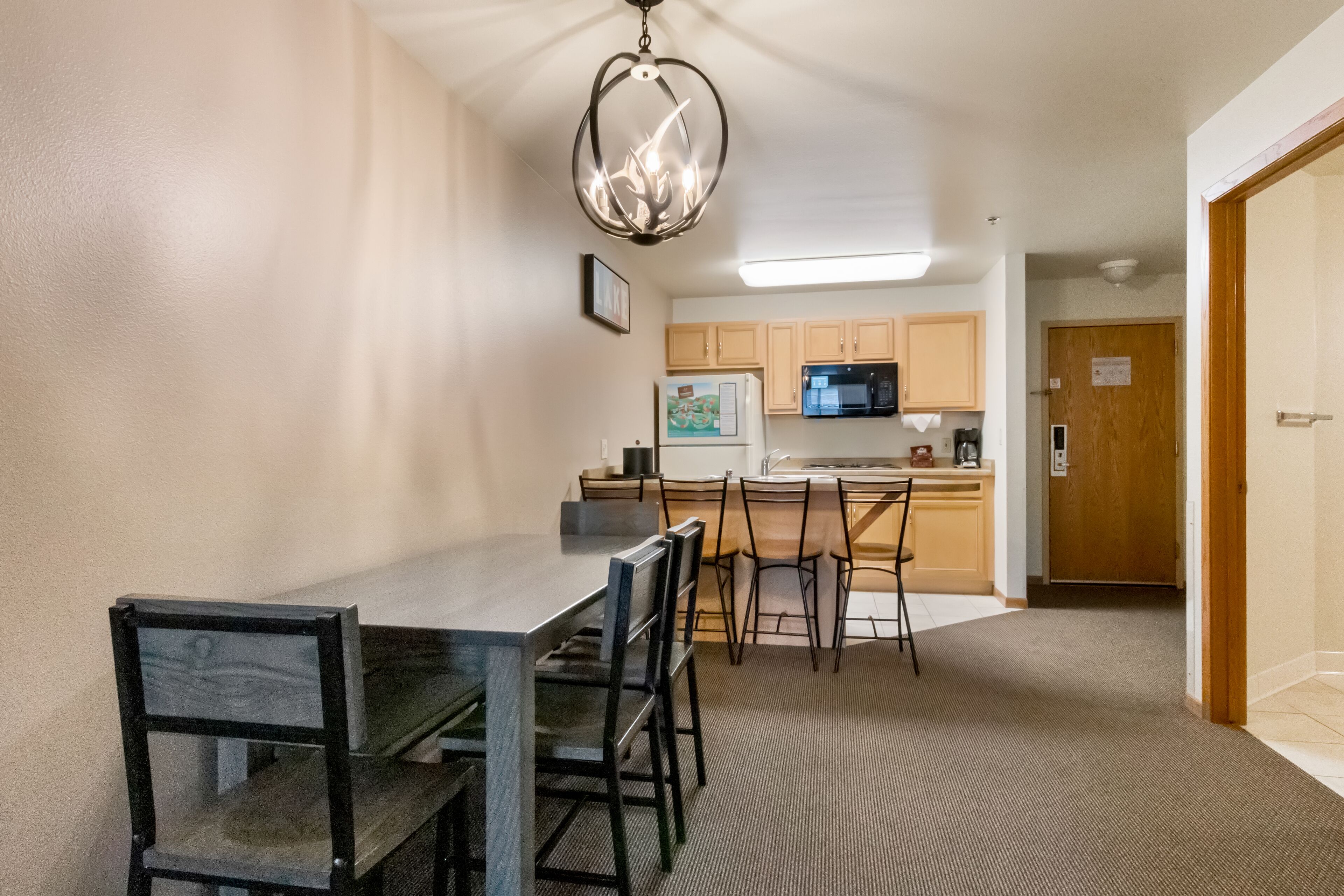 A compact kitchen with a dining area, featuring a chandelier, wooden cabinets, and a refrigerator.
