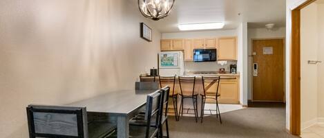 A compact kitchen with a dining area, featuring a chandelier, wooden cabinets, and a refrigerator.